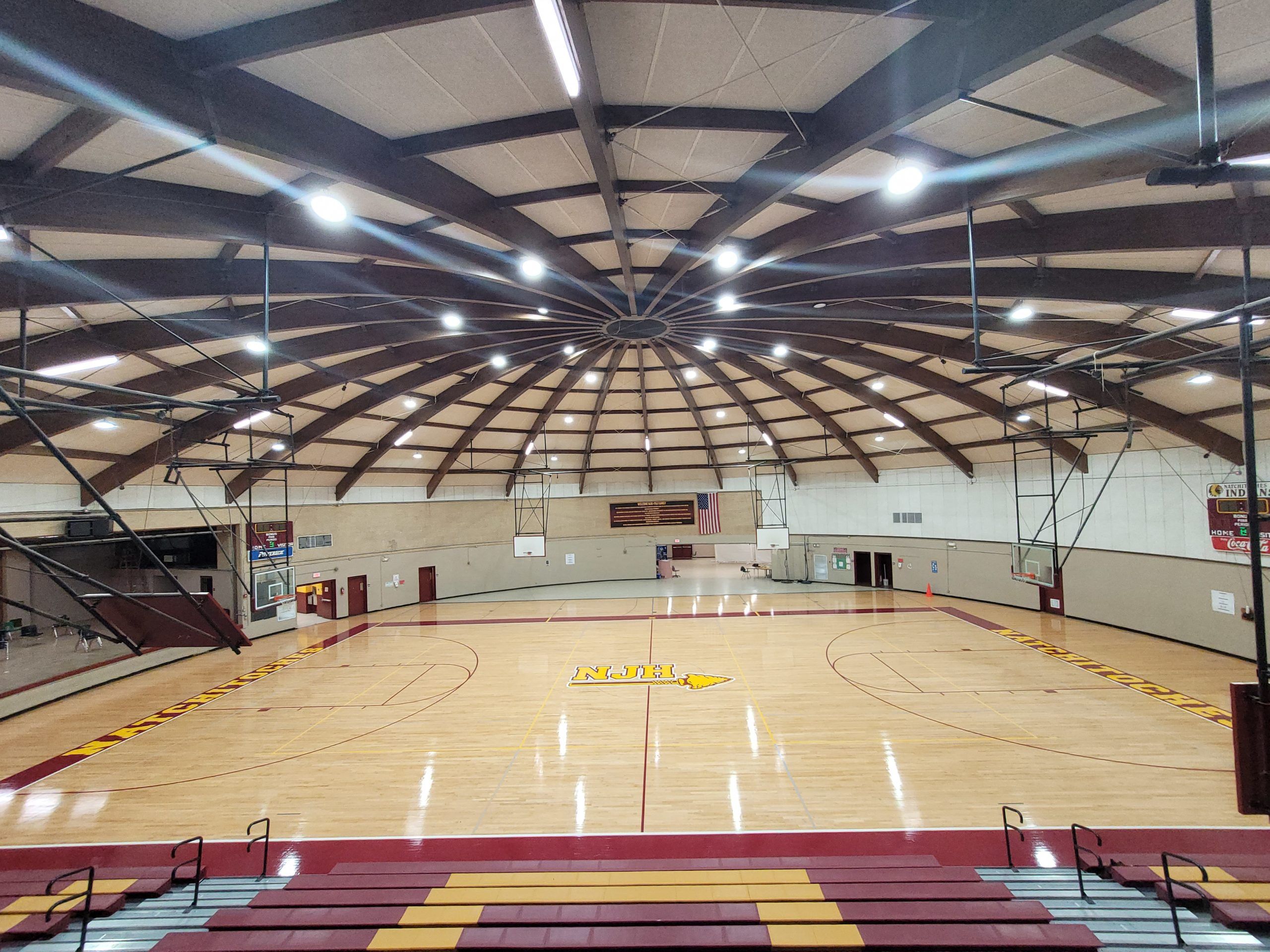 Glossy refinished hardwood basketball court under a domed, wood-beamed gym ceiling with maroon and gold sidelines and painted center lettering, showing Sports Floors, Inc. basketball floor refinishing in Memphis, TN