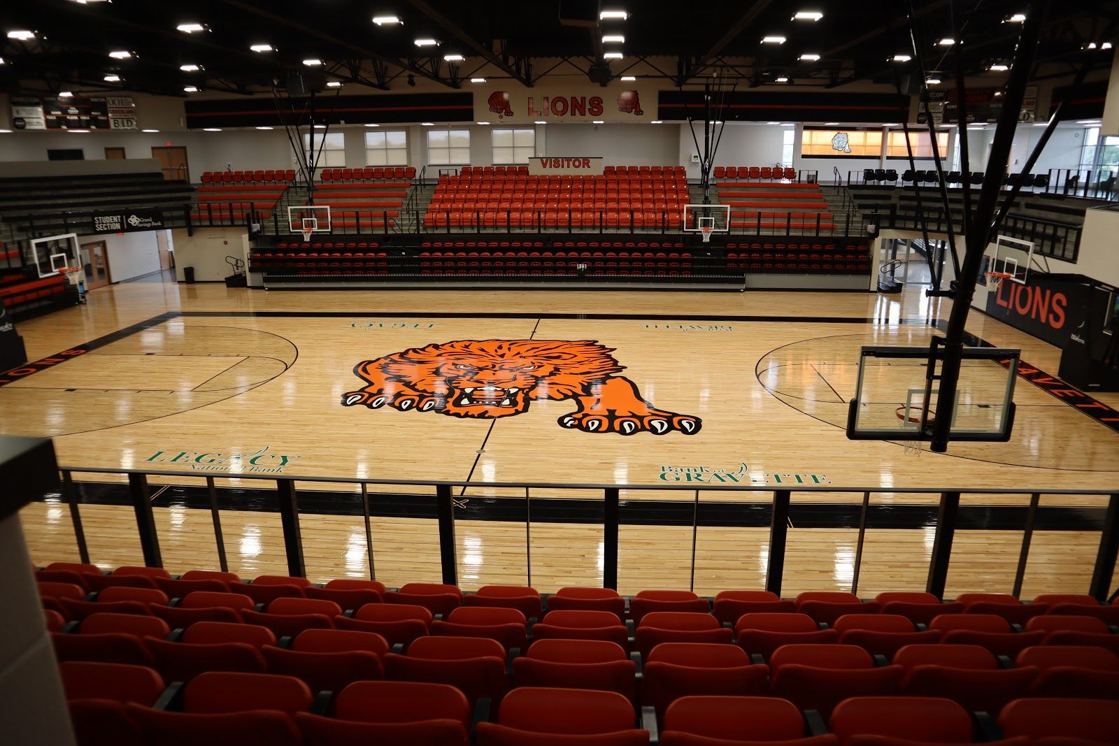 Gravette High School gym with a hardwood basketball court installed by Sports Floors, Inc., an orange lion logo at center court, and red bleachers