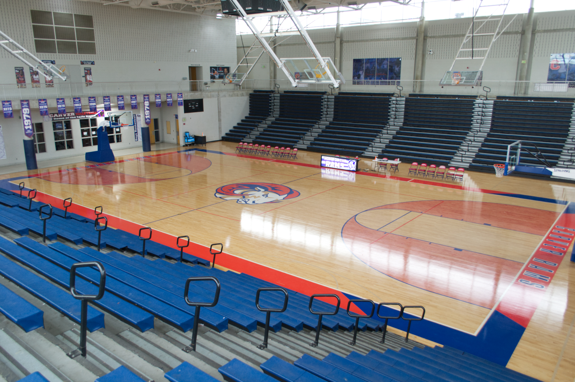High school arena basketball court with a fresh finish, a painted center-court mascot logo, red-shaded keys, and blue bleachers, showing Sports Floors, Inc. basketball floor refinishing in Memphis, TN