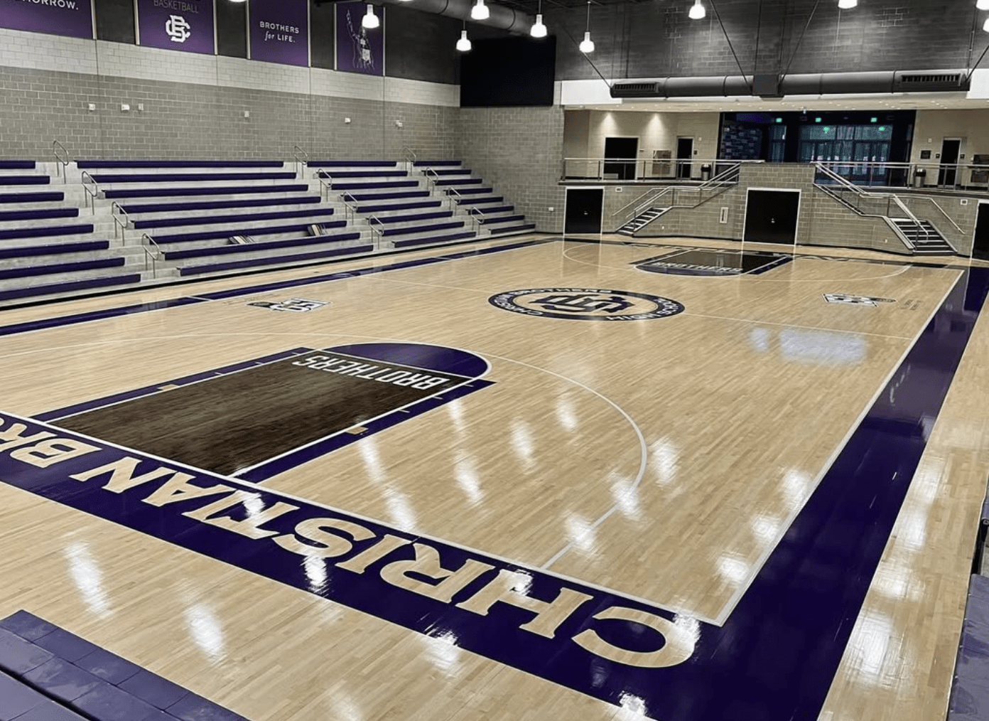 Newly finished hardwood basketball court by Sports Floors, Inc. at Christian Brothers High School in Memphis, with a glossy maple finish, purple “Christian Brothers” sideline lettering, a stained “Brothers” lane and a center-court logo